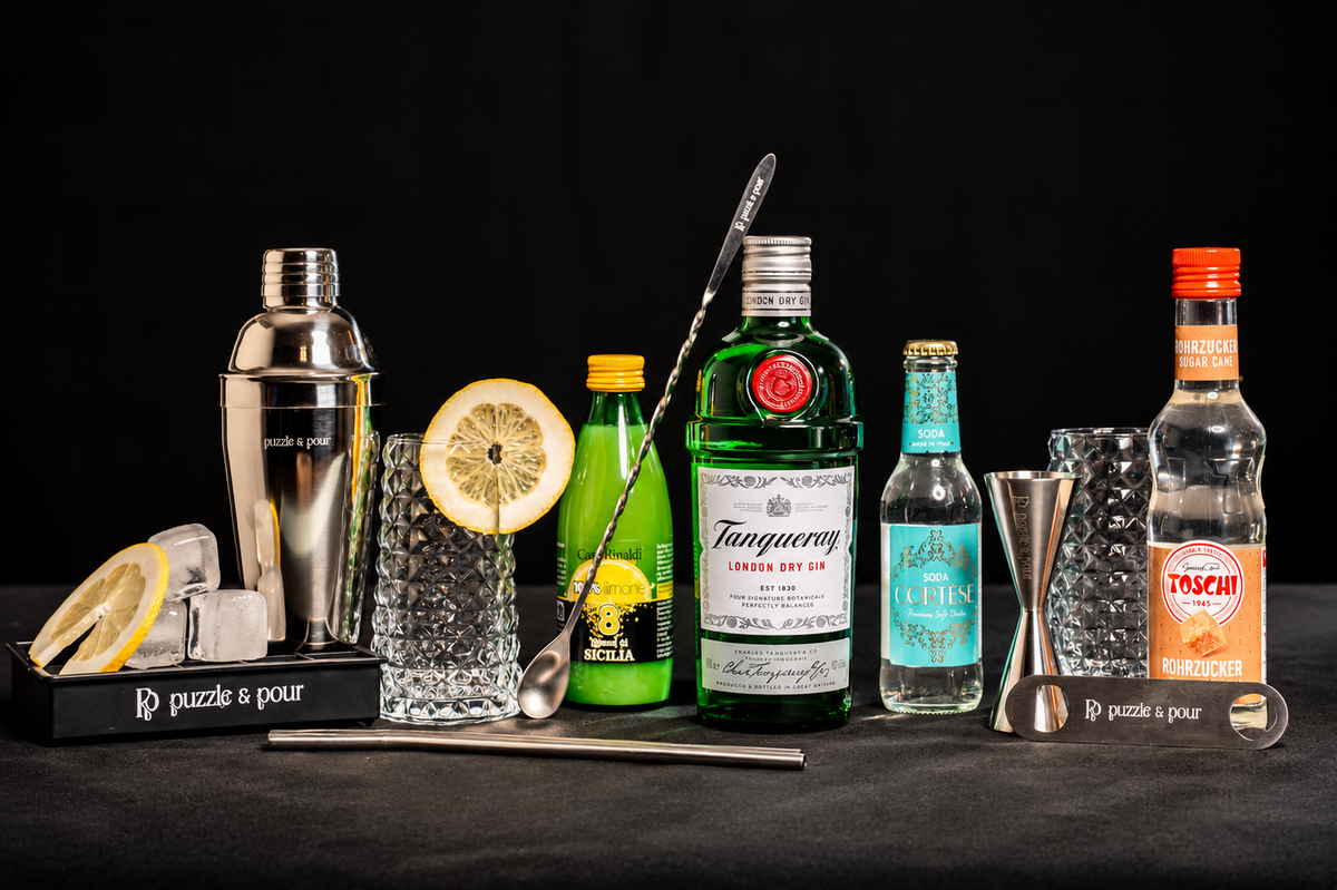 Tanqueray Gin Fizz Premium Box di Puzzle & Pour con Tanqueray London Dry Gin, Soda Cortese, succo di limone, sciroppo Toschi, due bicchieri e attrezzatura professionale da bartender. Kit cocktail completo e idea regalo originale per gli amanti del gin e della mixology.